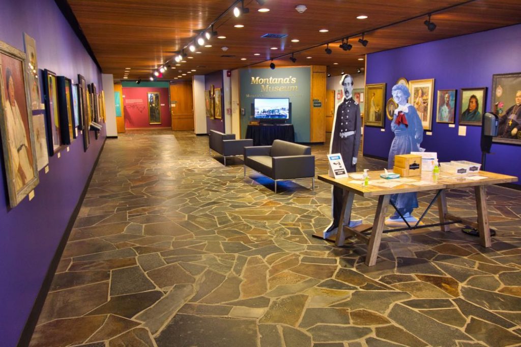 Museum interior with cardboard cutouts of historic figures and Native American portrait paintings on a purple wall.