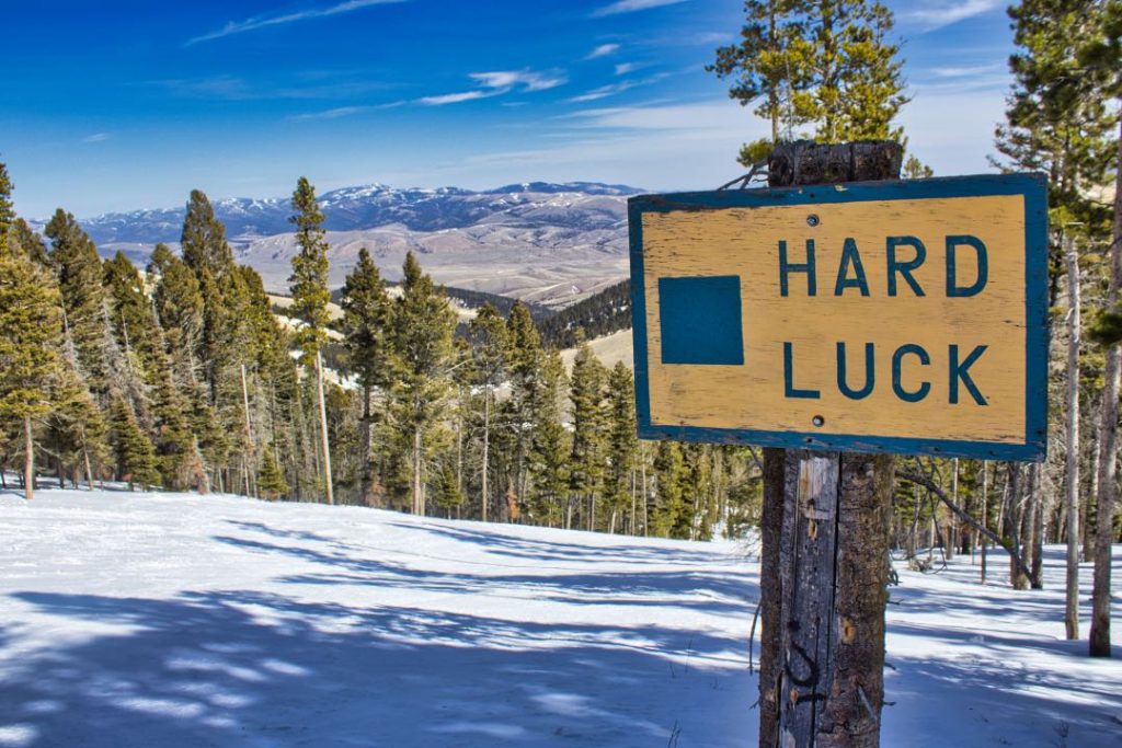 Snowy ski slope with trail sign stating "Hard Luck"