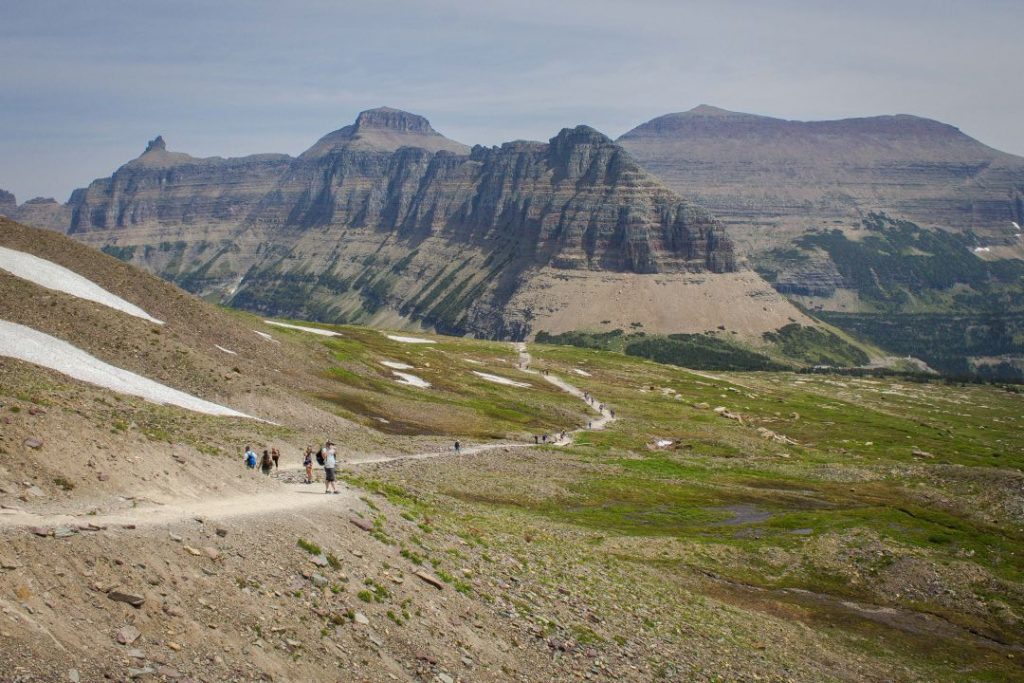Several hikers on a trail winding through a treeless landscape with a large mountain ridge in the background.