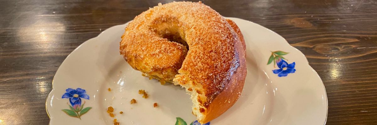 A spiral-shaped pastry with a bite taken out of it sits on a white plate with blue flowers painted on it.