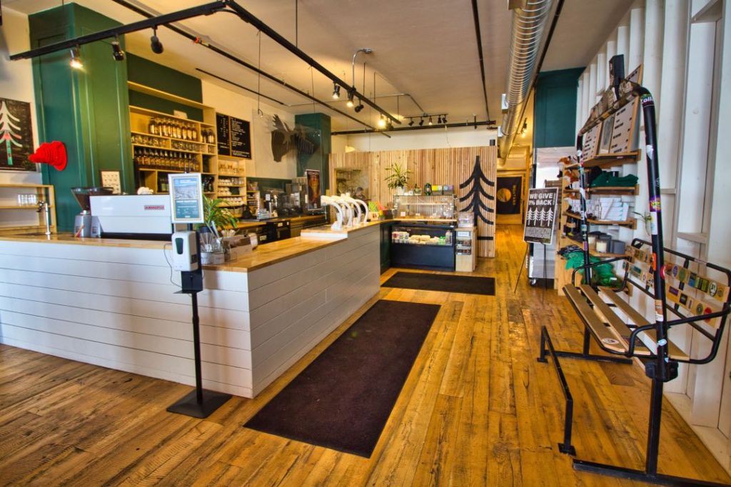 Interior of a modern coffee shop with white tile walls and hardwood floors. A decomissioned chairlift chair functions as a bench next to the counter.