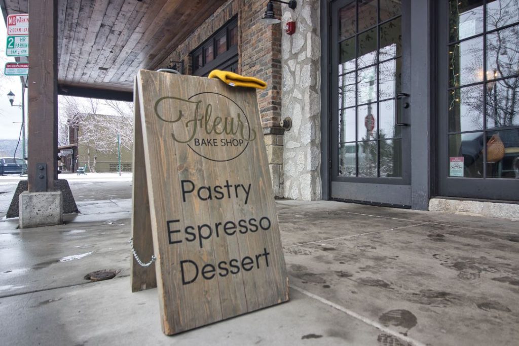 A wooden signboard announcing "Fleur Bake Shop: Pastry, Espresso, Dessert" sits on the sidewalk outside a glass storefront.