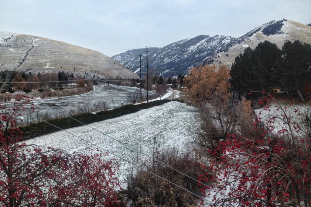 An icy river winds its way through a valley with mostly leafless trees and a grey sky.