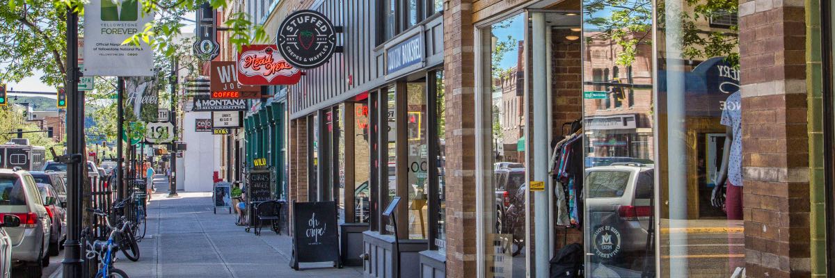 Looking down a sidewalk with several storefront sporting neon-signs in a small town.