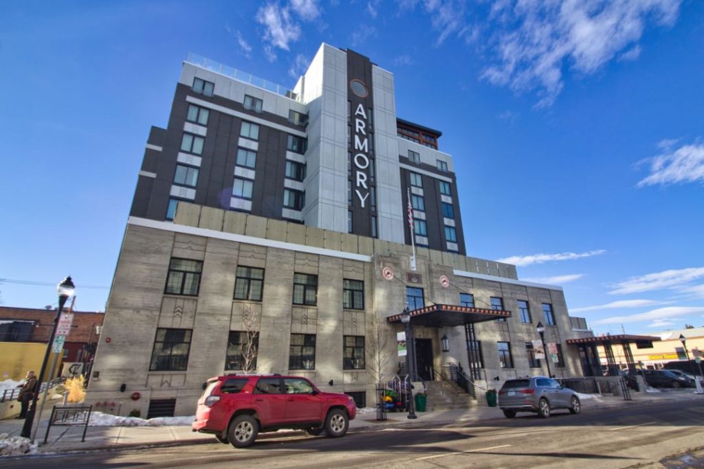 The ten story concrete hotel with the word "Armory" on the side. A few SVUs are parked on the street in front of the hotel.