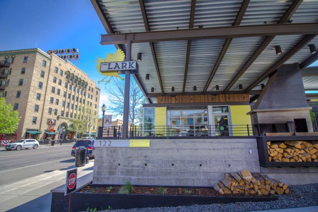 An aluminum awning extends over a concrete patio with a stock of split logs for an outdoor fire pit.