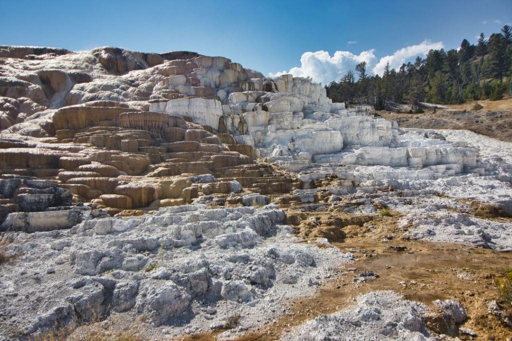 A cascade of white and orange rock is covered with a shiny coating from a hot spring.