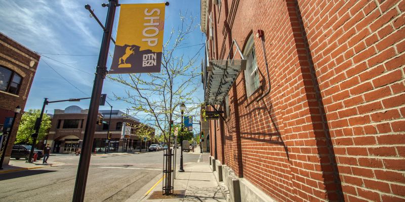 A lamp post with a yellow and brown banner that says "Shop DTN BZN" next to a brick building.