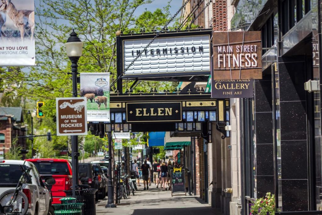 A sidewalk with numerous streetsigns with bicycles leaned against them. Above the sidewalk is a sign for the theater that says "Ellen".