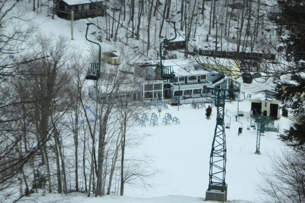 A single chair lift ascending a hill with a ski lodge in the background.