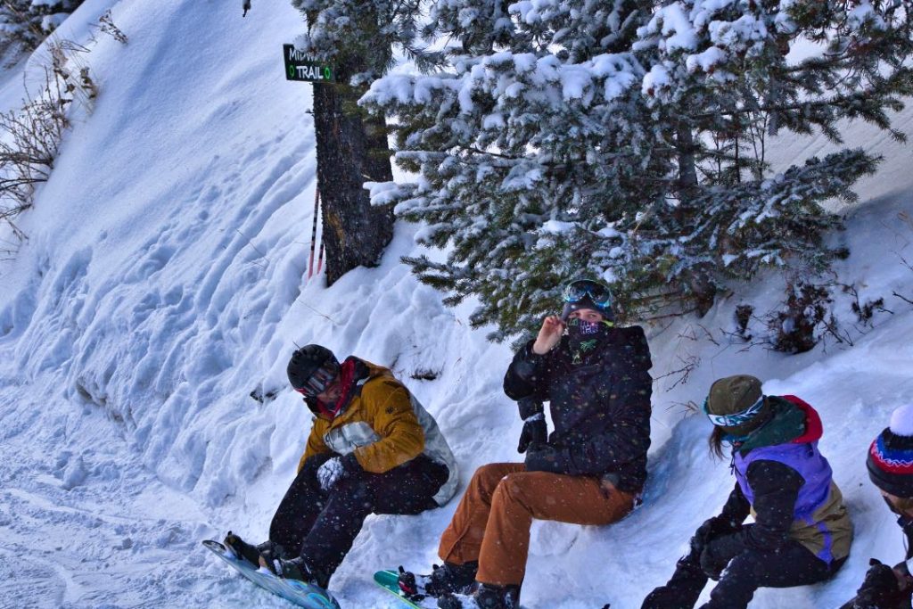 Four young snowboarders clip into the boards after getting off the lift.
