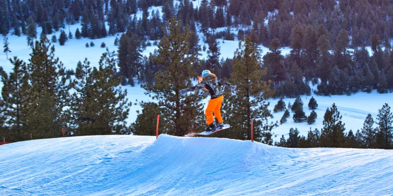 A snowboarder in orange pants launches off a jump.