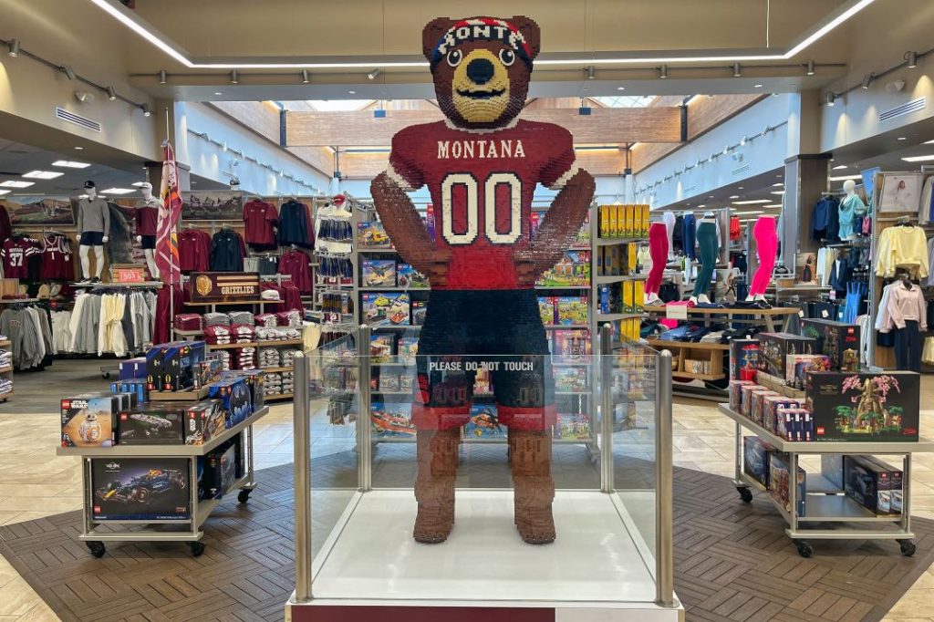 A bear mascot wearing a University of Montana jersey, made out of legos, in the middle of a sporting goods store.